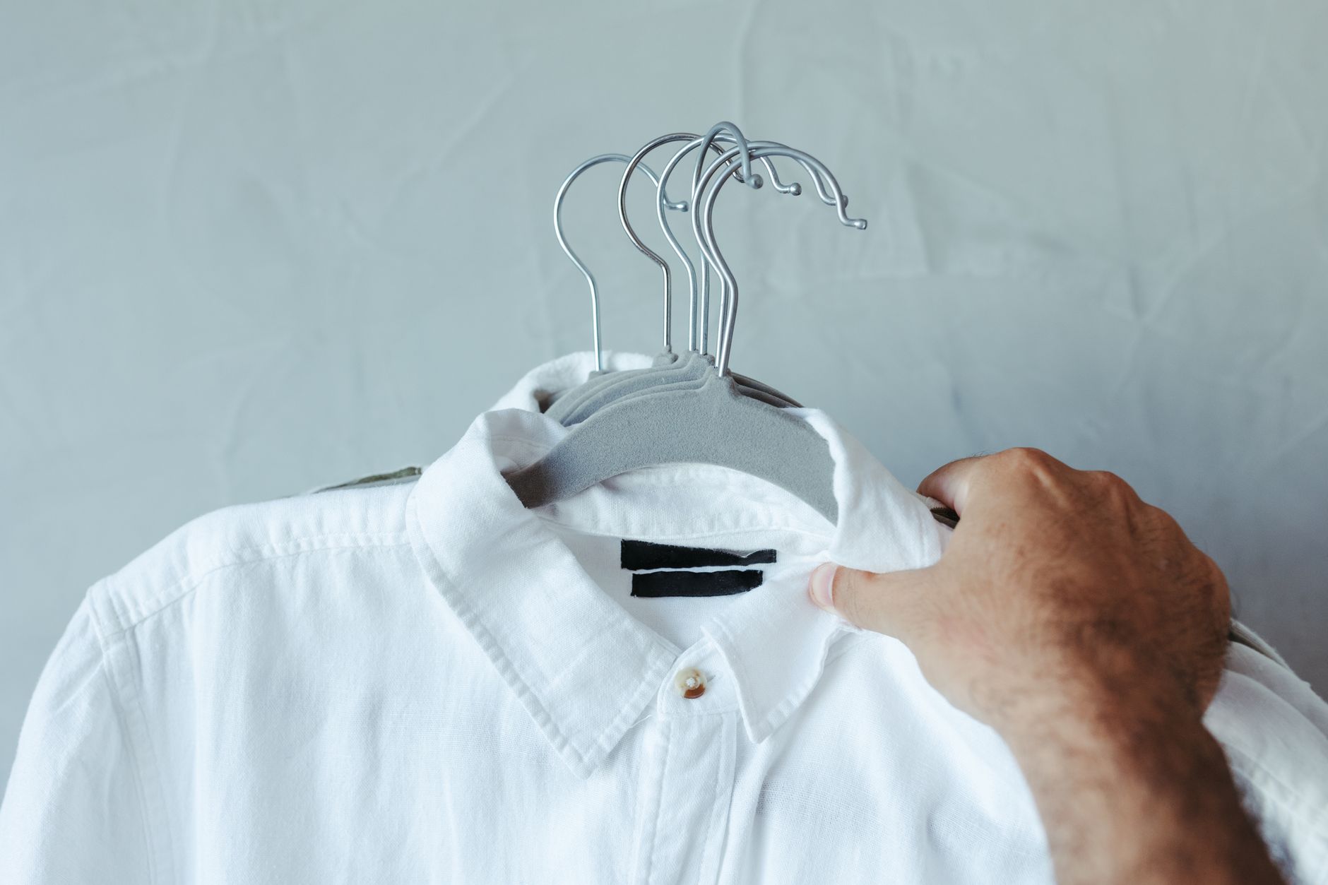 Primer plano de una camisa blanca en percha sostenida por una mano